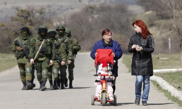 Жени разхождат малко дете пред погледа на въоръжени руски военни край столицата на Крим &ndash; Симферопол. Обстановката в региона остава крайно напрегната 2 дни преди референдума за съдбата на автономната република. Снимка: Reuters