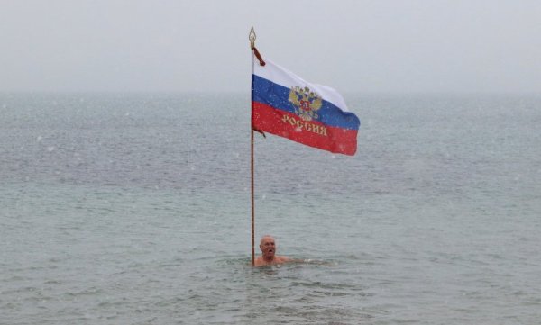 Любител на зимното плуване се къпе във водите на Черно море край Крим с руското знаме в ръце. Снимка: Reuters